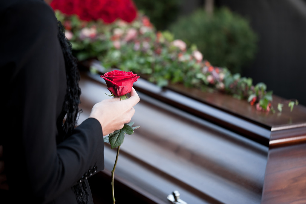 Person holding a rose with a coffin in the background.