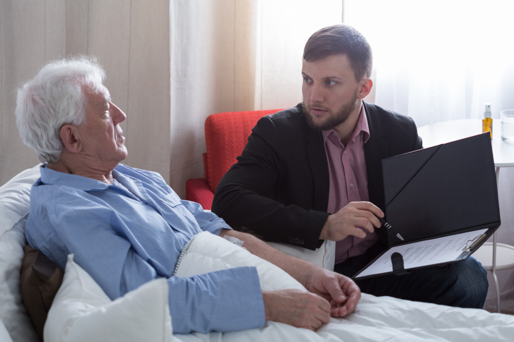 An old man on a hospital bed talking to his estate administrator to prepare his last will and estate