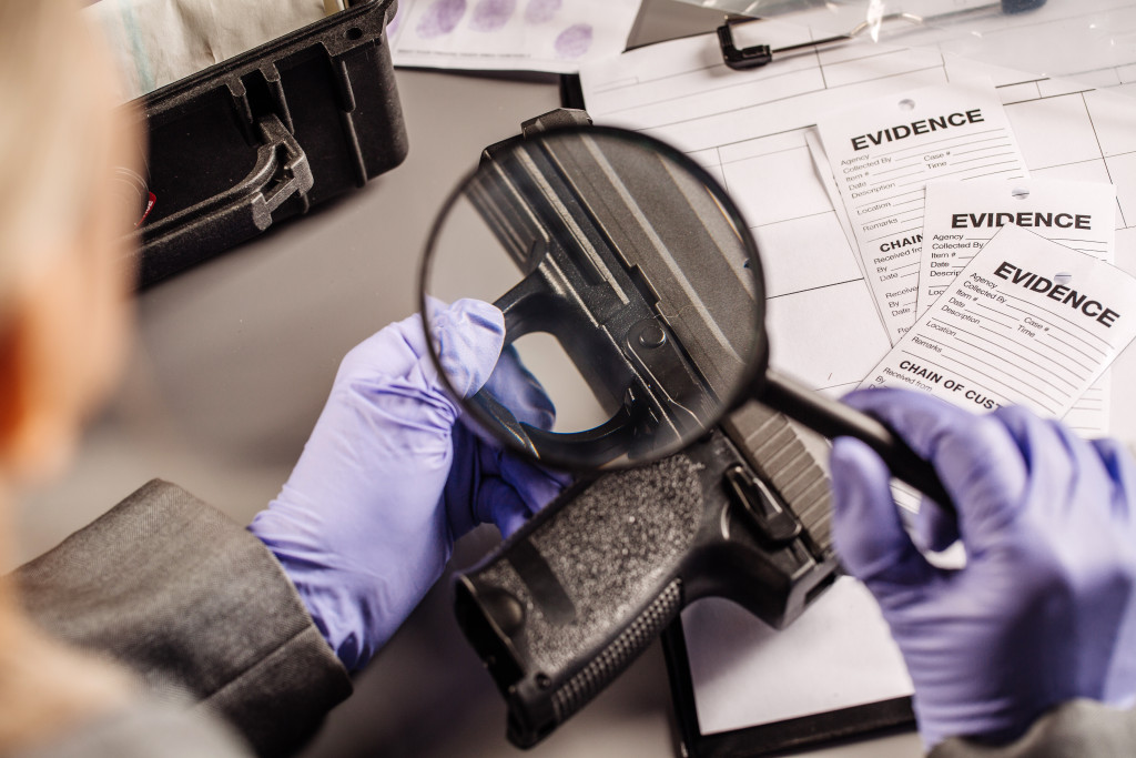 forensic specialist using magnifying glass to investigate a gun found in discovery